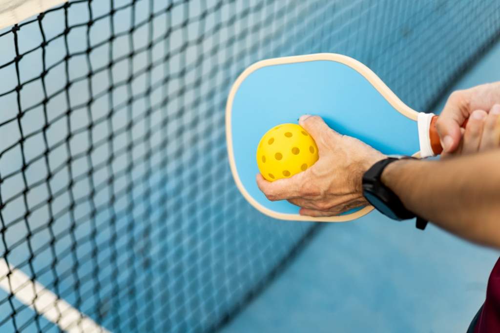 person holding pickleball paddle and ball in front of the net