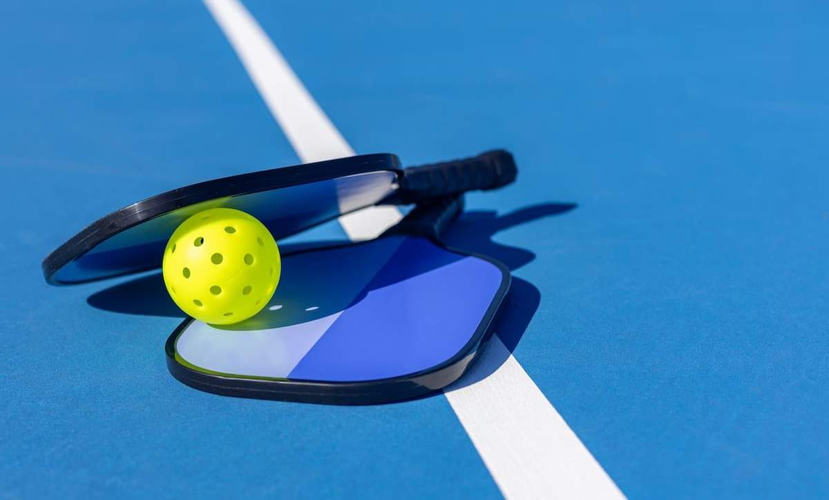 Fun Denver date night activity featuring pickleball paddles and a yellow ball on a professional blue court at Pickleball Food Pub.