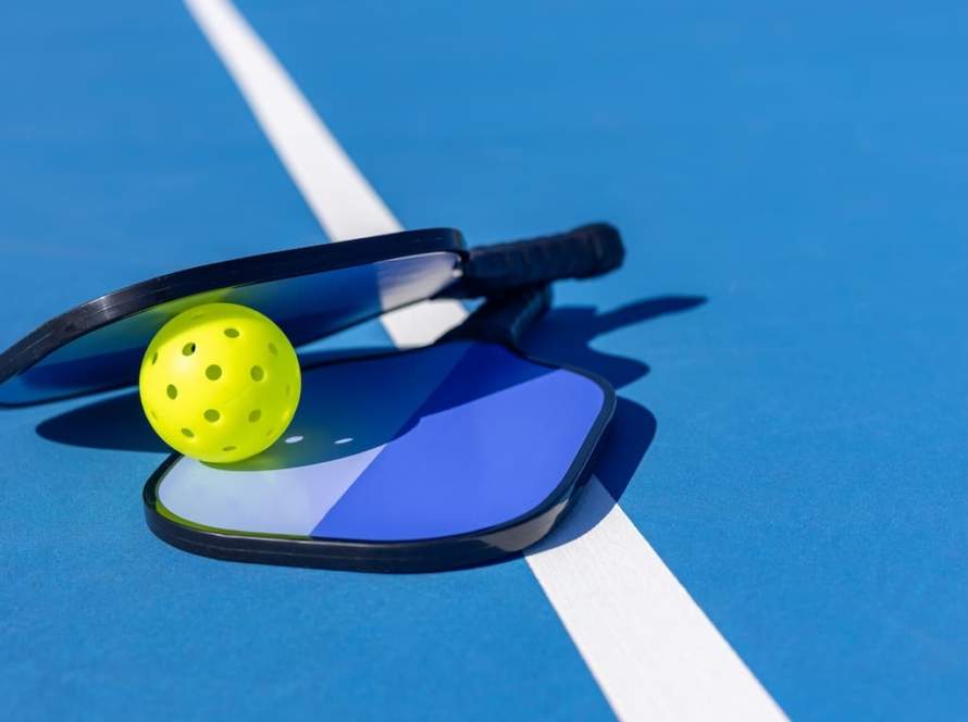 Fun Denver date night activity featuring pickleball paddles and a yellow ball on a professional blue court at Pickleball Food Pub.